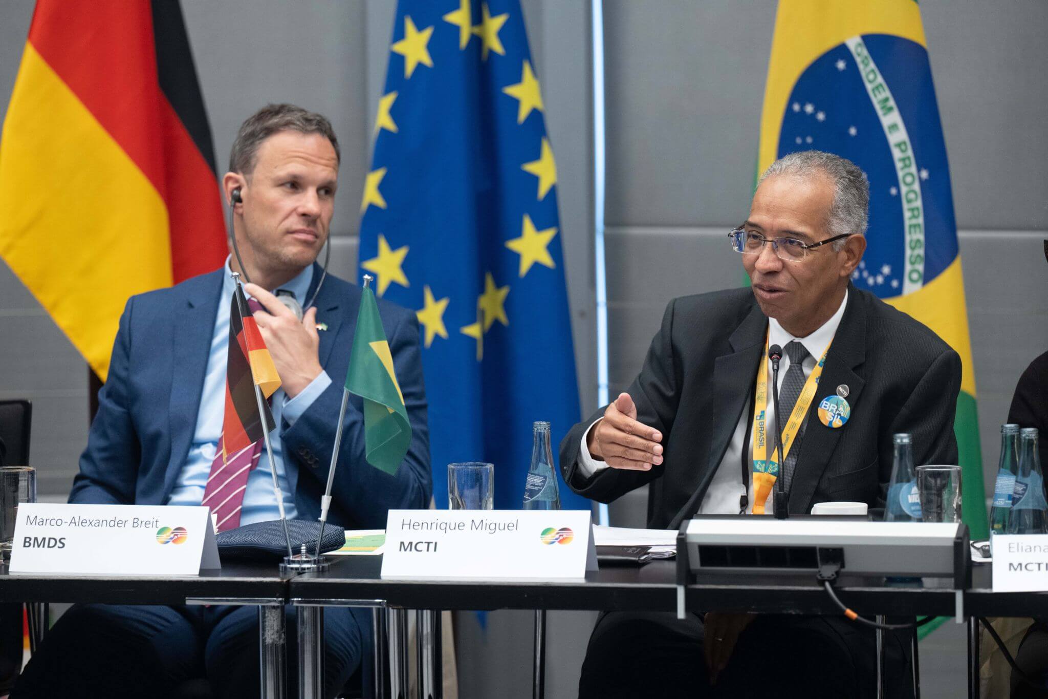 The photo shows Henrique Miguel from MCTI and Marco-Alexander Breit from BMDS, sitting in front of a German, Brazilian and European flag.